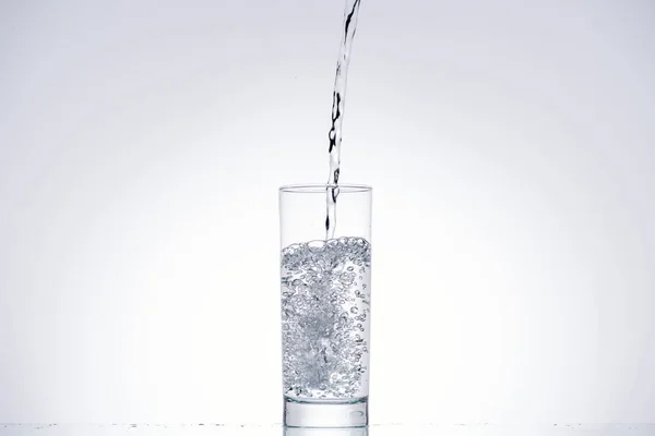 Wasser im Trinkglas auf weißem Hintergrund mit Hintergrundbeleuchtung — Stockfoto