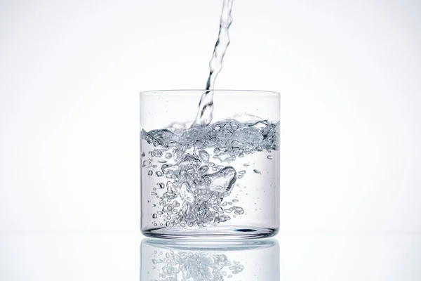 Agua vertiendo en vaso de beber sobre fondo blanco con retroiluminación - foto de stock