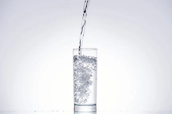 Fond de l'eau versant dans le verre sur blanc avec rétro-éclairé et espace de copie — Photo de stock
