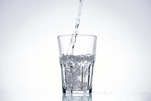 Фон з водою, що ллється в склянці на білому з підсвічуванням — Stock Photo