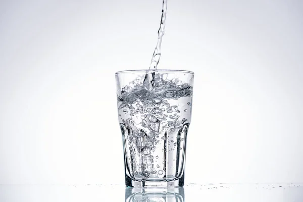 Agua vertiendo en vaso de beber sobre fondo blanco con retroiluminación y espacio de copia - foto de stock