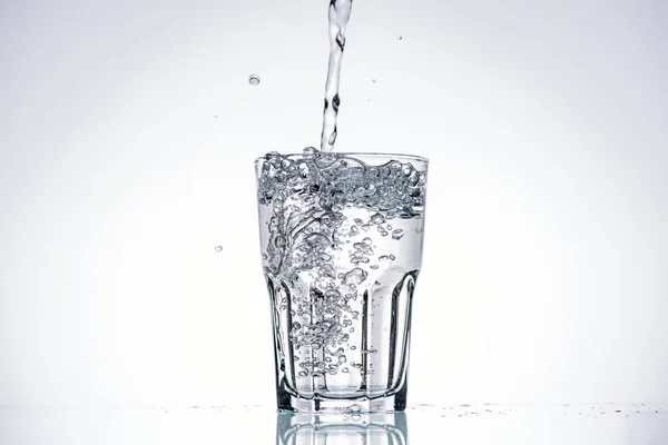 Wasser gießt in Trinkglas auf weißem Hintergrund mit Hintergrundbeleuchtung und Kopierraum — Stockfoto