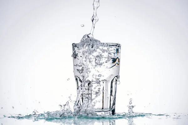 Wasser in vollem Glas auf weißem Hintergrund mit Hintergrundbeleuchtung und Spritzern — Stockfoto