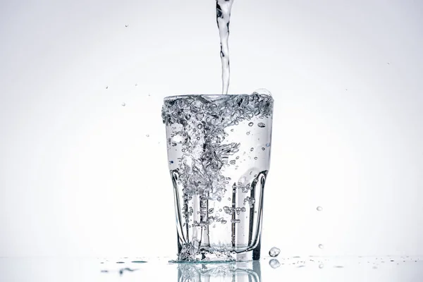 Wasser in vollem Glas auf weißem Hintergrund mit Hintergrundbeleuchtung und Spritzern — Stockfoto