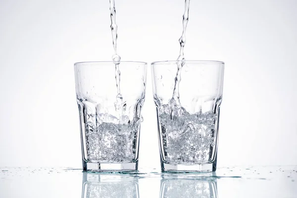 Água derramando em copos no fundo branco com retroiluminado — Fotografia de Stock