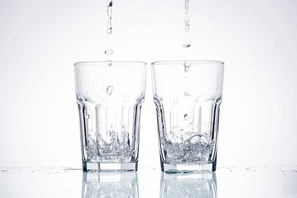 Water pouring in glasses on white background with backlit — Stock Photo