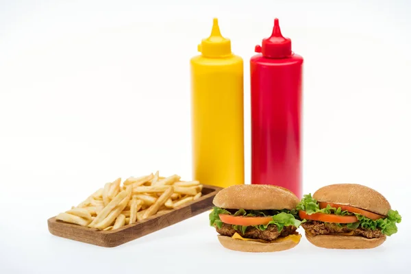 Hambúrgueres de frango perto de batatas fritas e garrafas com mostarda e ketchup isolado em branco — Fotografia de Stock