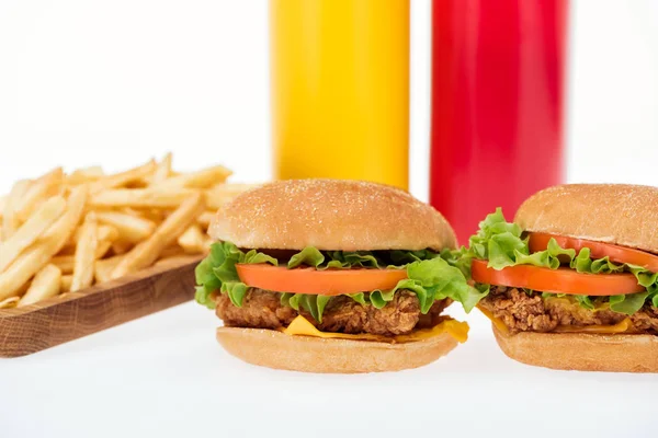 Foco selectivo de sabrosas hamburguesas de pollo cerca de papas fritas y botellas aisladas en blanco - foto de stock