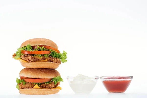 Tasty chicken burgers near glass bowls with ketchup and mayonnaise isolated on white — Stock Photo