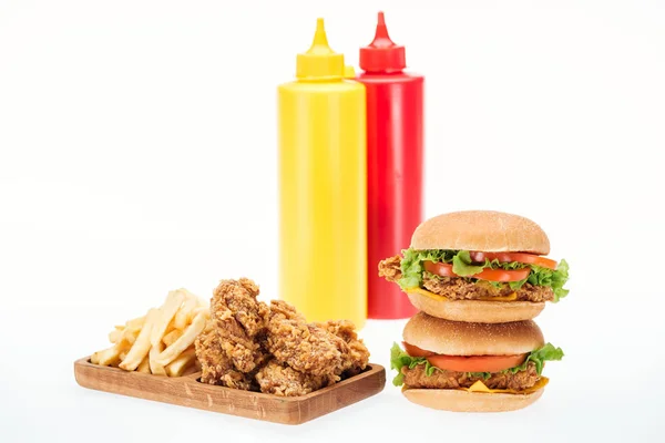 Crispy chicken nuggets, hamburgers and french fries near bottles with ketchup and mustard isolated on white — Stock Photo