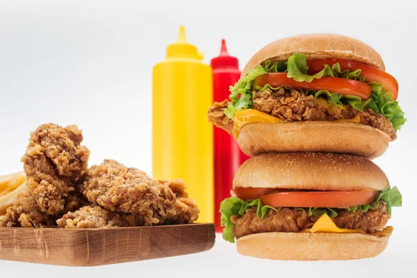 Messa a fuoco selettiva di croccanti pepite di pollo e hamburger di pollo vicino a bottiglie con ketchup e senape isolati su bianco — Foto stock