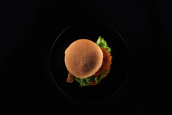 Вид сверху на вкусный нездоровый куриный бургер на тарелке изолированы на черном — стоковое фото