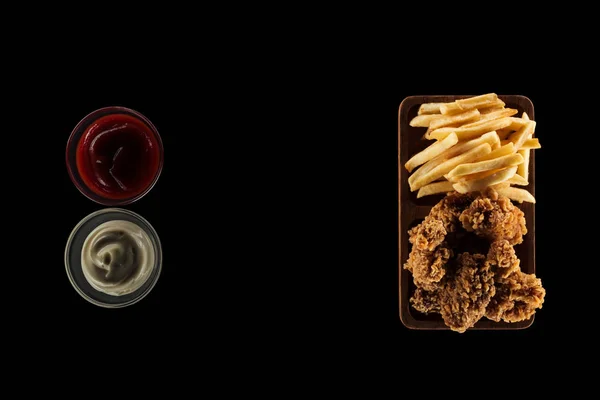 Vista superior de saborosas batatas fritas e nuggets de frango crocante perto de maionese e ketchup isolado em preto — Fotografia de Stock