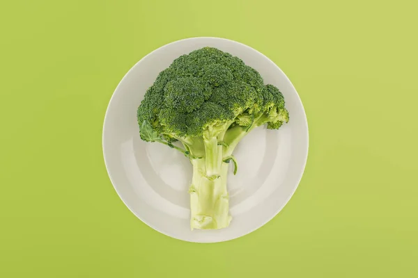 Top view of organic ripe broccoli on white plate isolated on green — Stock Photo