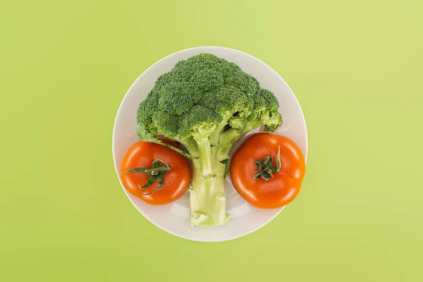 Vista superior de brócolis maduros orgânicos perto de tomates vermelhos na placa branca isolada em verde — Fotografia de Stock