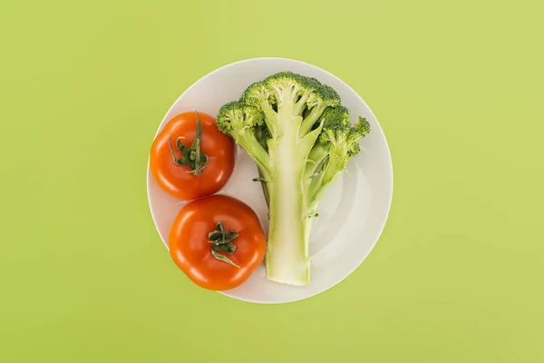 Top view of red tomatoes near organic broccoli on white plate isolated on green — Stock Photo