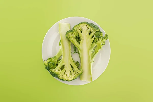 Top view of tasty organic broccoli on white plate isolated on green — Stock Photo