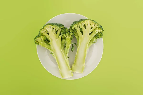 Top view of tasty organic broccoli on white plate isolated on green — Stock Photo