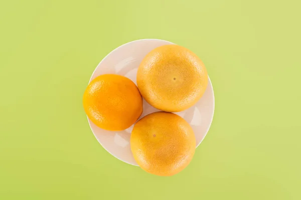 Top view of whole orange and grapefruits on white plate isolated on green — Stock Photo