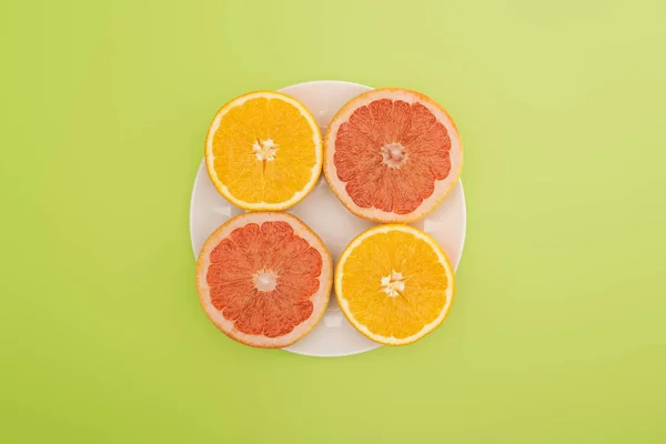 Draufsicht auf geschnittene Orangen und Grapefruits auf weißem Teller isoliert auf grünem Teller — Stockfoto