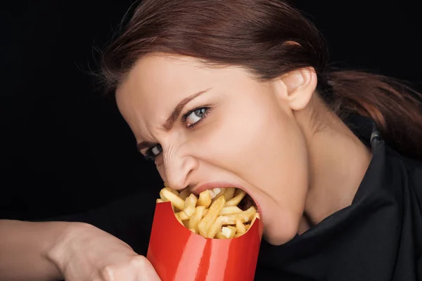 Mulher emocional comer batatas fritas salgadas enquanto olha para a câmera isolada no preto — Fotografia de Stock