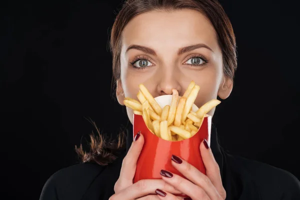 Mulher cobrindo rosto com batatas fritas enquanto olha para a câmera isolada no preto — Fotografia de Stock