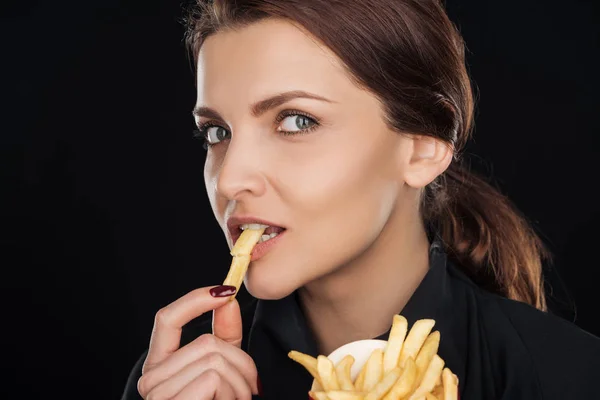 Attractive while eating tasty french fry isolated on black — Stock Photo