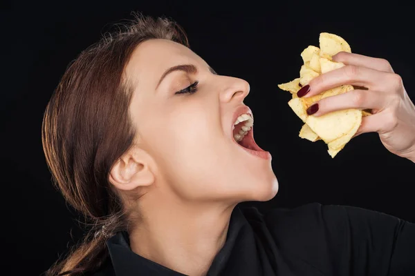 Mulher atraente comer batatas fritas crocantes isolado no preto — Fotografia de Stock