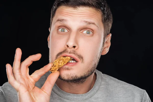 Handsome man eating chicken nugget while looking at camera isolated on black — Stock Photo