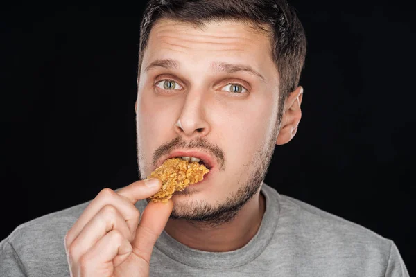 Bonito homem comer saboroso frango nugget enquanto olhando para câmera isolada no preto — Fotografia de Stock