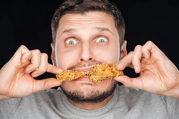 Emotionaler Mann isst Chicken Nuggets, während er isoliert auf Schwarz in die Kamera schaut — Stockfoto