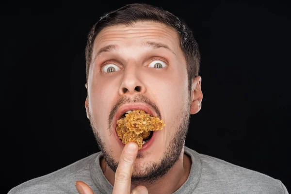 Mann steckt Chicken Nuggets in den Mund, während er die Kamera isoliert auf schwarz anschaut — Stockfoto