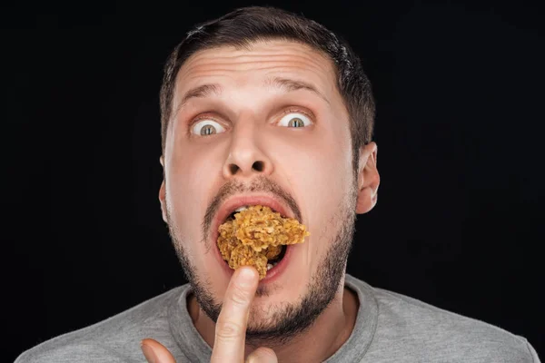 Homme mettre dans la bouche poulet pépites tout en regardant caméra isolé sur noir — Photo de stock