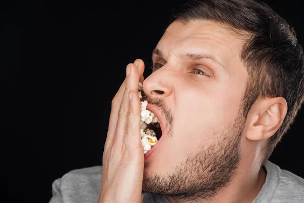 Man eating salty popcorn isolated on black — Stock Photo