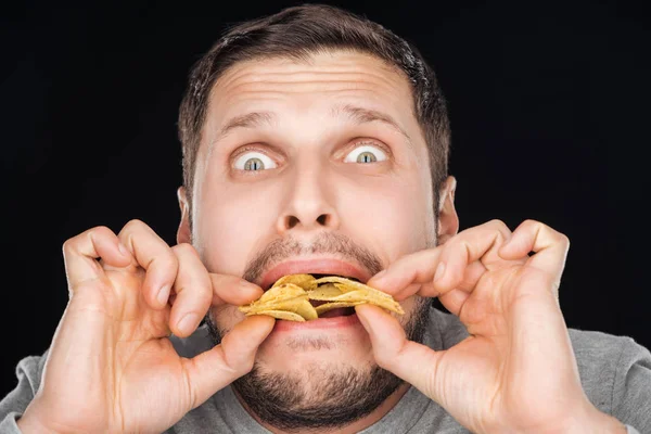 Emotionab mal comer chips enquanto olha para a câmera isolada no preto — Fotografia de Stock