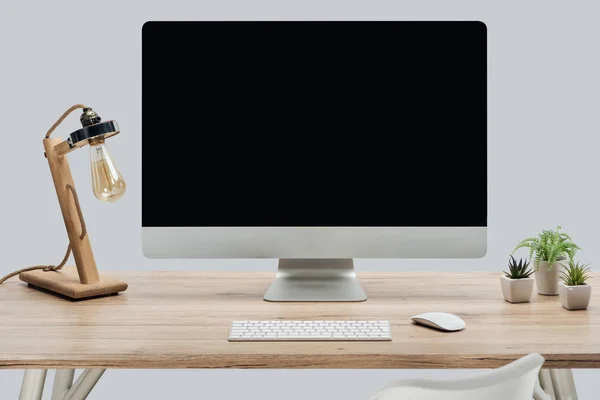 Moderno lugar de trabajo con monitor de ordenador con pantalla en blanco, lámpara y plantas verdes en escritorio de madera aislado en gris - foto de stock