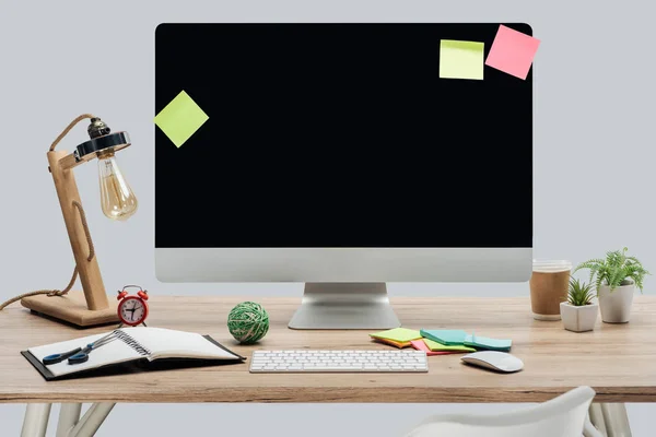 Local de trabalho moderno com monitor de computador, notas pegajosas e artigos de papelaria em mesa de madeira isolados em cinza — Fotografia de Stock