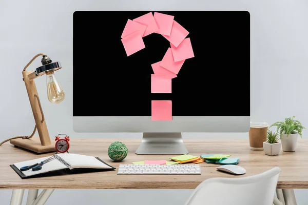 Modern workplace with pink question mark made of sticky notes on computer monitor and stationery at wooden desk isolated on grey — Stock Photo