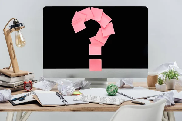 Modern workplace with pink question mark made of sticky notes on computer monitor, stationery and crumpled papers at wooden desk isolated on grey — Stock Photo