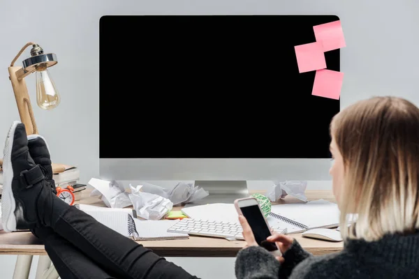 Вибірковий фокус дівчини, що сидить на безладному робочому місці і використовує смартфон ізольований на сірому — стокове фото