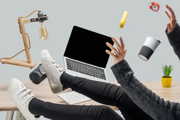 Cropped view of woman levitating in air with laptop and stationery at workplace isolated on grey — Stock Photo