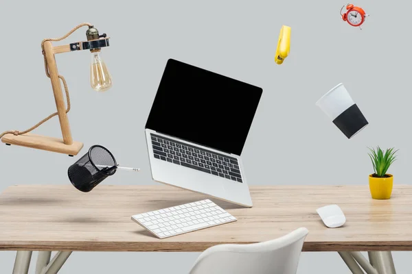 Laptop mit leerem Bildschirm und Schreibwaren, die in der Luft schweben, am Arbeitsplatz isoliert auf grau — Stockfoto