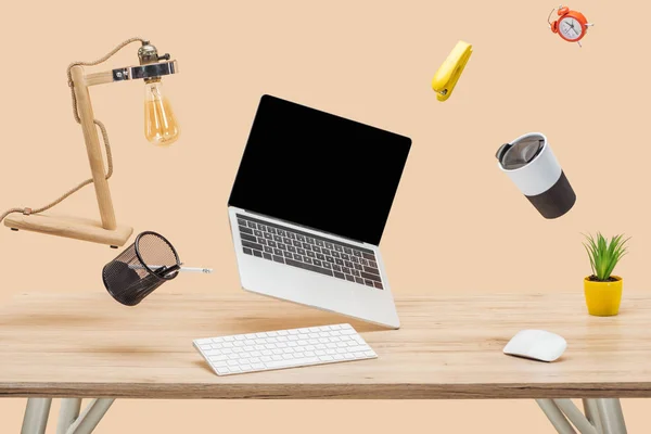Laptop mit leerem Bildschirm und Schreibwaren, die in der Luft schweben, am Arbeitsplatz isoliert auf beige — Stockfoto