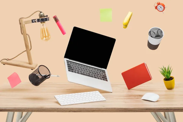 Laptop com tela em branco, lâmpada, notas pegajosas e papelaria levitando no ar acima da mesa de madeira isolada em bege — Fotografia de Stock