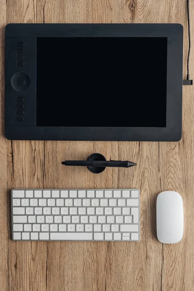Vista superior de la tableta gráfica, la pluma gráfica, el teclado inalámbrico de la computadora y el ratón de la computadora en la mesa de madera - foto de stock