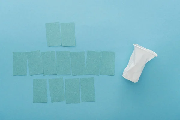 Vista superior de la taza de plástico blanco y notas adhesivas vacías sobre fondo azul - foto de stock