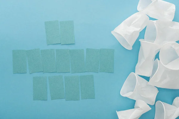 Draufsicht auf weiße Plastikbecher und leere Haftnotizen mit Kopierraum auf blauem Hintergrund — Stockfoto