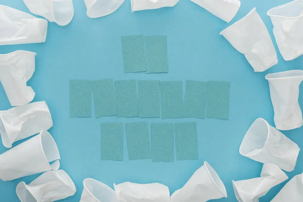 Vue du dessus des gobelets en plastique blanc et des notes collantes vides avec espace de copie sur fond bleu — Photo de stock