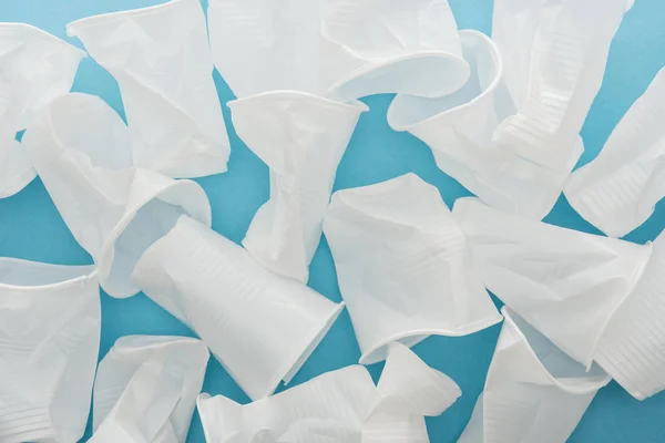 Вид сверху на белый и скомканные пластиковые чашки на синем фоне — стоковое фото