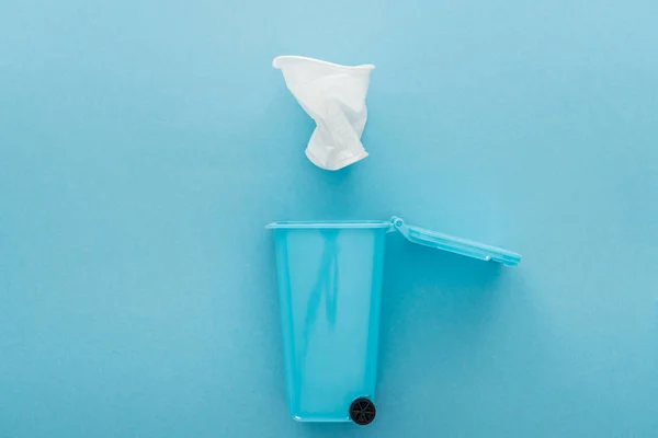 Vue du dessus de la tasse en plastique froissée blanche tombant dans la poubelle jouet sur fond bleu — Photo de stock